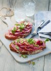Zwei Scheiben Brot mit Salami und Kräutern auf hellem Holzbrett — Stockfoto