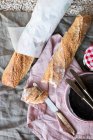 Pão francês em um pano de linho com um jarro de engarrafamento e facas e pratos — Fotografia de Stock