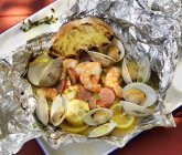Seafood cooked in foil with corn on the cob and grilled bread — Stock Photo