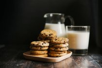 Stacks of cookies with chocolate and milk in glass and pitcher — Stock Photo