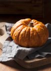 A munchkin pumpkin on a rustic wooden background with a grey linen napkin — Stock Photo