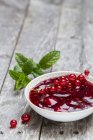 Red jam in bowl with redcurrants and mint on wooden surface — Stock Photo