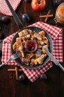 Пирожные с яблочным соусом и жареными сливами в чугунной сковороде на красно-белой ткани — стоковое фото