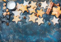 Gingerbread Christmas star shaped cookies with cinnamon, anise, nuts, baking molds and sugar powder on dark plywood painted background — Stock Photo