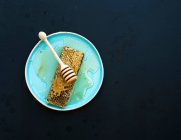 Honeycomb with honey dipper on blue ceramic plate over black background, top view copy space — Stock Photo
