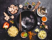 El arreglo del wok y los ingredientes para el plato oriental de fideos (visto de arriba) - foto de stock