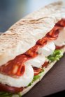 A sandwich with mozzarella, spicy salami, lettuce and tomatoes — Stock Photo