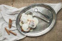 Zimtrollen mit Frischkäse-Zuckerguss und Zimtstangen auf einem silbernen Teller — Stockfoto