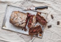 Cherry brownie with almond and dark chocolate cut into pieces on a silver tray over a piece of beige linen fabric — Stock Photo