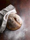 Frisch gebackenes Brot mit weißem Tuch und Mehl auf Holzoberfläche — Stockfoto