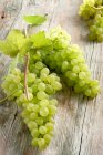 Grüne Trauben auf hölzernem Hintergrund mit Weinblättern — Stockfoto