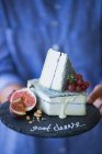 Козий сыр с инжиром и виноградом на каменной тарелке в руках — стоковое фото