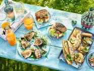Uma mesa colocada em um jardim com sanduíches e bebidas — Fotografia de Stock