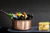 A copper saucepan of mussels with prawns, corn and vegetables served with a stack of chunky chips — Stock Photo
