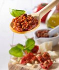 Tomato pesto and basil leaves on a wooden spoon above a wooden board with basil and dried tomatoes — Stock Photo