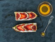 Fig. e sanduíches de queijo de cabra de morango com mel na superfície de pedra escura — Fotografia de Stock