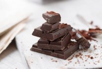 Stacked pieces of chocolate with cocoa powder on a chopping board — Stock Photo