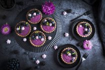 Blackberry yoghurt tartlets with mint leaves and meringue drops on black plates — Stock Photo