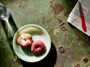 Персики на тарелке рядом с газетой и фруктовым ножом — стоковое фото