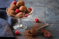 Chocolate truffles with fresh raspberries on glass stand and table — Stock Photo