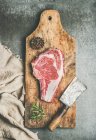 Pose plate de viande de bœuf cru de première qualité côte à côte de steak d'âge sec sur os avec assaisonnement et couteau à hachoir — Photo de stock