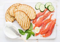 Grilled bread slices, smoked salmon, cottage cheese, cucumber and basil — Photo de stock