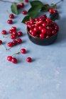 Ripe red cherries in ceramic bowl and on concrete surface — Stock Photo