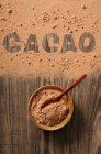 Cacao in polvere in una ciotola e versato su uno sfondo di legno con la parola 'cacao' — Foto stock