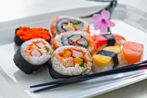Assortment of makis and sushis on white plate with chopsticks — Stock Photo