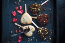 Herzförmige vegane Kuchen auf Sticks, dekoriert mit dunkler Bierglasur, gefriergetrockneten Erdbeeren und Pistazien — Stockfoto