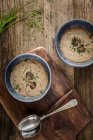 Duas taças de sopa de cogumelos grossa e cremosa decoradas com fatias de cogumelos e cebolinha em tigelas azuis em uma superfície de madeira — Fotografia de Stock