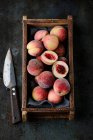 Свежие персики в деревянной коробке и ноже — стоковое фото