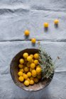 Mirabelle plums in wooden bowl with herbs and on gray cloth — Stock Photo