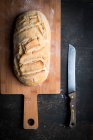 Хліб ручної роботи на дерев'яній дошці з ножем на темній поверхні — стокове фото