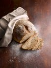 Fresh baked bread, slices with flour and cloth on wooden surface — Stock Photo