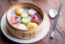Surtido y colorido dim sum dumplings en un vapor de bambú en la mesa de madera con palillos - foto de stock