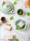 Pasteles de té verde Matcha con glaseado de chocolate blanco y semillas de sésamo con una taza de té verde y bálsamo, hojas de menta. - foto de stock
