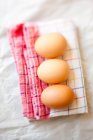 Fresh eggs on checkered tea towel — Stock Photo