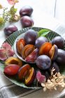 Prunes fraîches dans des bols métalliques avec des plantes et des feuilles — Photo de stock