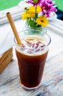 An balinese iced coffee with an ecological bamboo straw on a table with flowers in the background — Stock Photo
