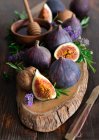 Figues fraîches entières et coupées en deux avec des noix, des herbes et du miel avec du bâton dans un bol sur une planche en bois — Photo de stock