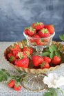 Frische Erdbeeren im Glas und auf Metallständer mit weißer Papierblume — Stockfoto