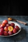 Prunes fraîches dans un bol, une coupée en deux et couteau sur le fond — Photo de stock