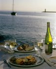 Zwei Teller mit Essen und Wein auf gedecktem Tisch am Meer — Stockfoto