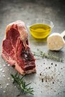 Raw Porterhouse steak with sprigs of herbs, pepper, sea salt, garlic and olive oil — Stock Photo