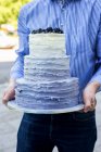 Un hombre sosteniendo un pastel de bodas de tres niveles - foto de stock