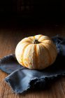 A munchkin pumpkin on a frayed, dark blue linen napkin — Stock Photo