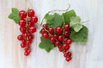 Groselhas vermelhas com folhas em uma superfície de madeira branca — Fotografia de Stock