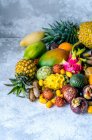 A large pile of assorted fresh and tasty tropical fruits on a gray background — Stock Photo