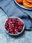 Frozen redcurrants and strawberries in ceramic bowl and oranges on background — Stock Photo